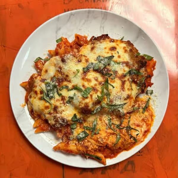 Baked ziti pasta with melted cheese, tomato sauce, and basil on a white plate.